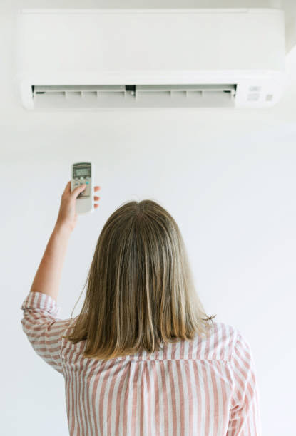 istock Woman holding remote control aimed at the air conditioner. 859735176