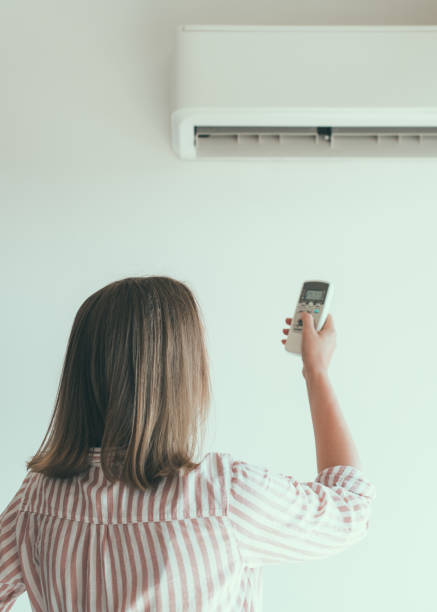 istock Woman holding remote control aimed at the air conditioner. 859735184