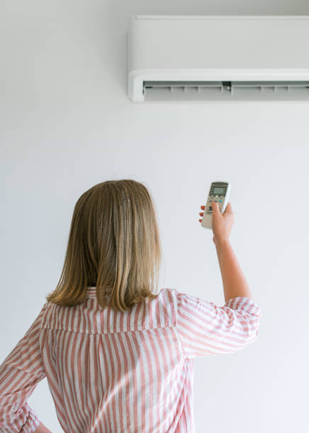 istock Woman holding remote control aimed at the air conditioner. 859735186