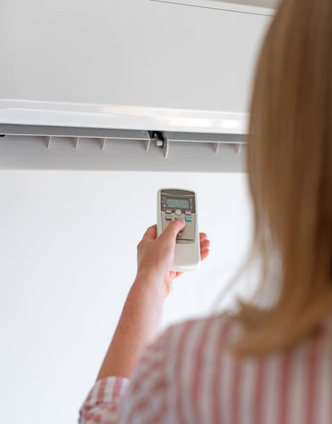 istock Woman holding remote control aimed at the air conditioner. 859735188