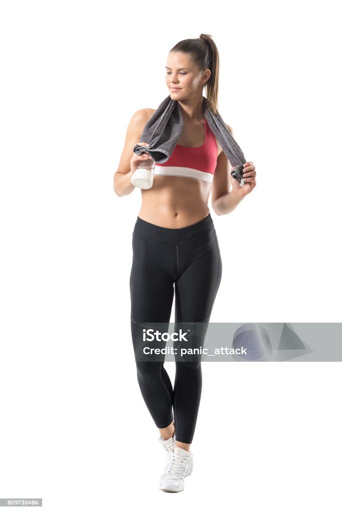 Fit healthy sporty woman with glass water bottle and towel around neck smiling Fit healthy sporty woman with glass water bottle and towel around neck smiling. Full body length portrait isolated on white background. 20-29 Years Stock Photo
