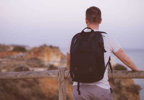 Male tourist with backpack looking at the ocean.