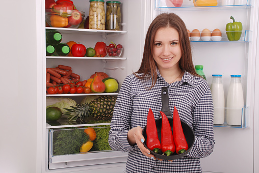 Portrait of a girl with a red hot pepper. A girl holding a red pepper near the fridge.