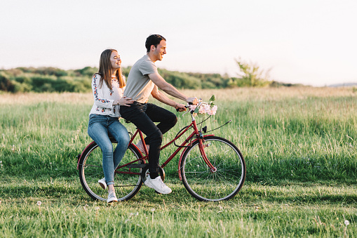 Smiling man cycling with woman walking on grassy field