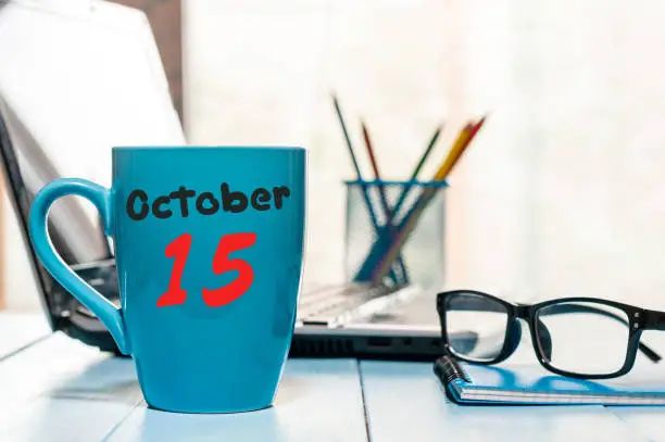 October 15th. Day 15 of month, hot coffee cup with calendar on accauntant workplace background. Autumn time. Empty space for text.