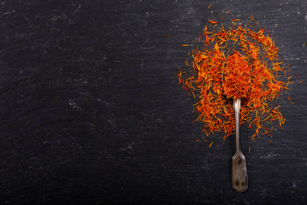 dried saffron spice in a spoon on dark background, top view