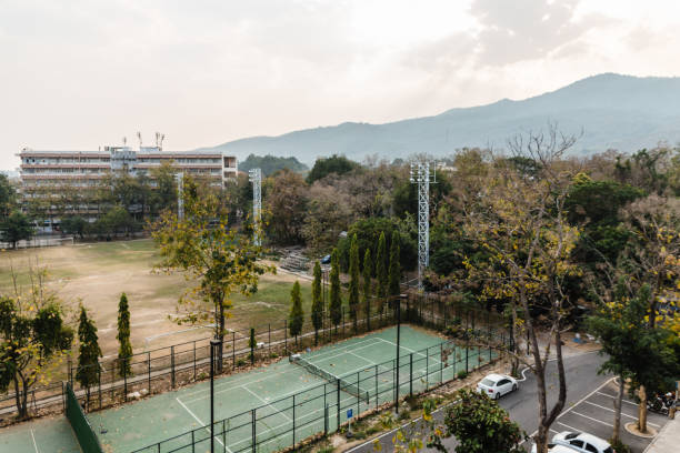 campo de ténis na escola com árvores, carros e montanha ao fundo em chiang mai, tailândia. - sunrise new zealand mountain range mountain - fotografias e filmes do acervo