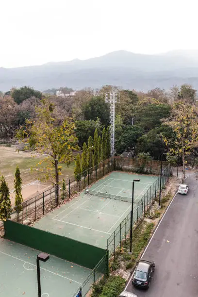 Tennis court in school with trees, cars and mountain in the background in Chiang Mai, Thailand.