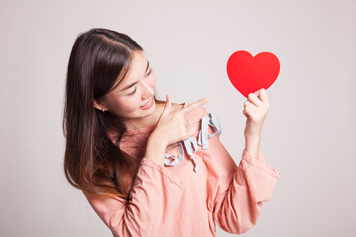 Asian woman point to red heart on gray background