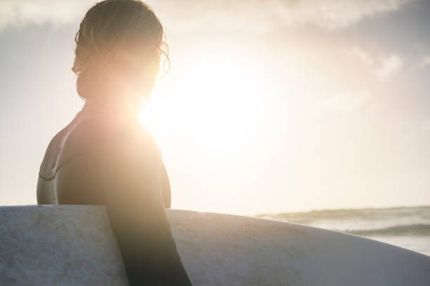 istock backlit surfer holding surfboard, with sunset lens flare 859814216
