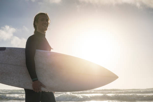 istock backlit surfer holding surfboard, with sunset lens flare 859814256