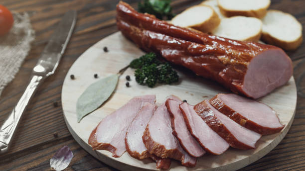 Piece of smoked Ham with some fresh herbs on wooden background stock photo