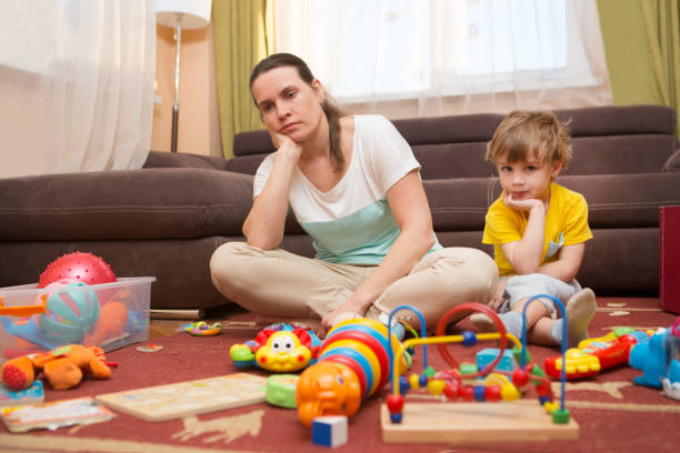 若い妊娠中の母親と幼い息子、自宅。母親と幼い息子は床の上に座る。お母さんは、家の上を片付けるに疲れています。子には、おもちゃが散らばっていた。家を混乱します。 - child beauty mother little boys ストックフォトと画像