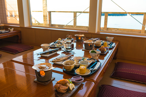 Breakfast table set richly with traditional Japanese food at sun rise. Lake in front of the window. Utoro, Japan.