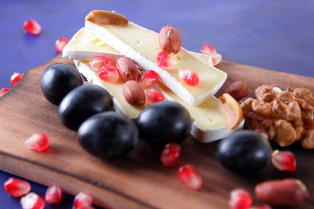 istock Camembert cheese, sliced cheese, peanuts, walnuts, pomegranate seeds on a wooden board on a dark blue background 859858132
