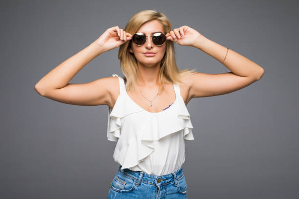 istock Young attractive lady in jeans and sunglasses posing in studio on grey background not isolated, blond girl hipster summer outfit concept, photo with place for text 859859994