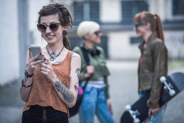 Three female friends, living alternative lifestyle, going together to skate park or music festival. Punkers and hipsters together, having fun and doing leisure activities. Redhead, blonde and girl with dreadlocks and tattoos sharing moments.