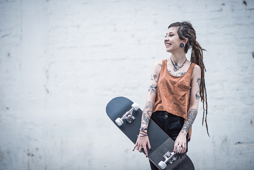 Portrait of hipster - punker young woman with tattoos and dreadlocks, piercings and jewelry. Unique beautiful young woman living alternative life, but still typical for millennial generation people. Young woman is going to skate park
