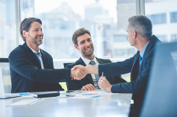 Businessmen shaking hands at the board room table. Businessmen shaking hands at the board room table. They are all wearing suits, and they are smiling and happy. They have just sealed a contract corporate boardroom stock pictures, royalty-free photos & images