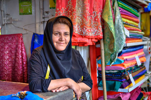 una donna iraniana matura in hijab vende tessuti nel bazar. - negoziante di tessuti foto e immagini stock