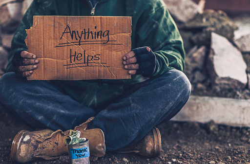 Fighting adversity. Homeless man with sign and money tin