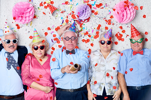 Pleased senior people lying on floor with confetti and paper balls tired from Christmas party, elderly senior man in the middle exploding party popper