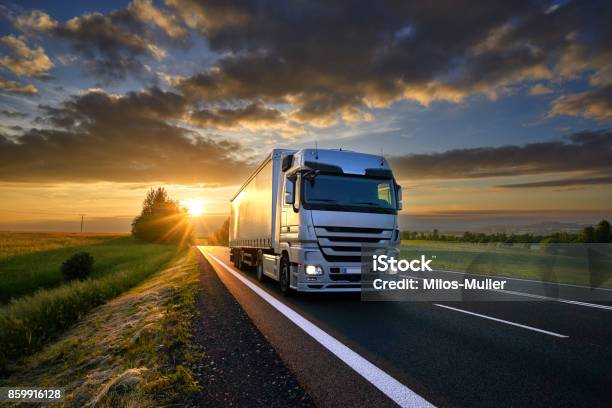 Lkwfahren Auf Der Asphaltstraße In Ländlichen Landschaft Bei Sonnenuntergang Mit Dunklen Wolken Stockfoto und mehr Bilder von Schweres Nutzfahrzeug