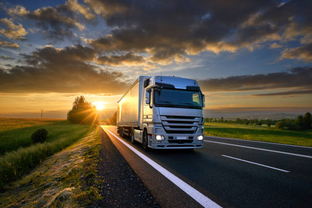 camion che guida sulla strada asfaltata nel paesaggio rurale al tramonto con nuvole scure - mezzo di trasporto foto e immagini stock