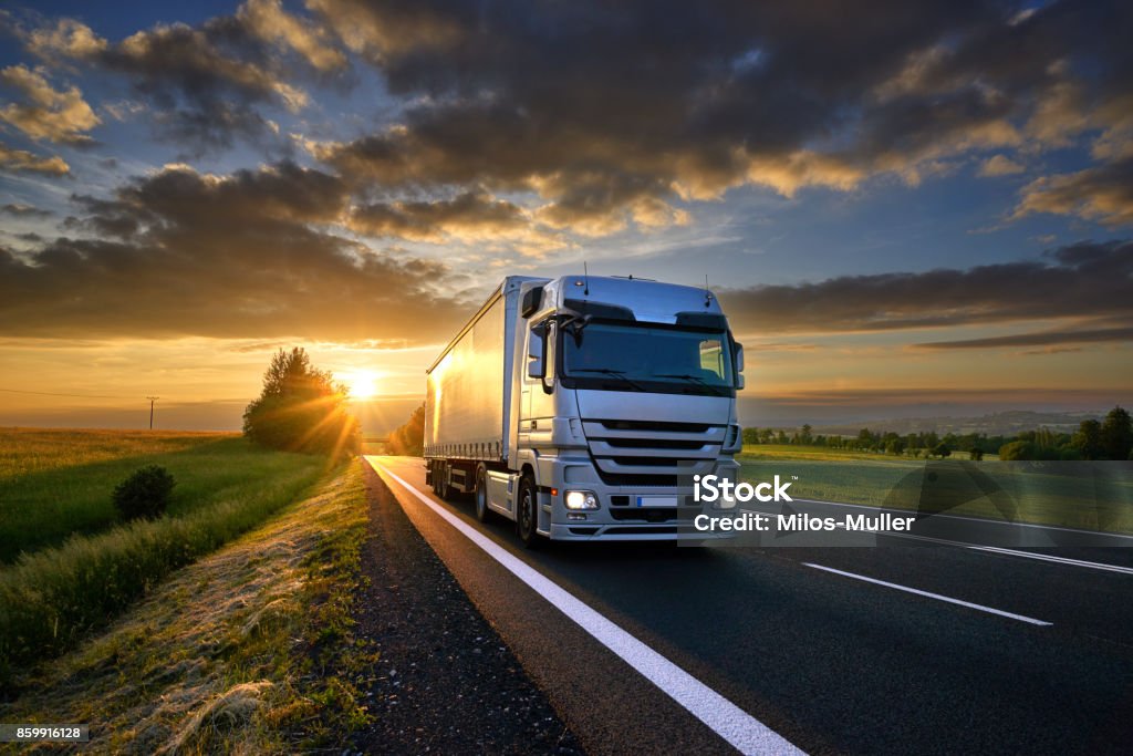 Truck driving on the asphalt road in rural landscape at sunset with dark clouds Truck Stock Photo