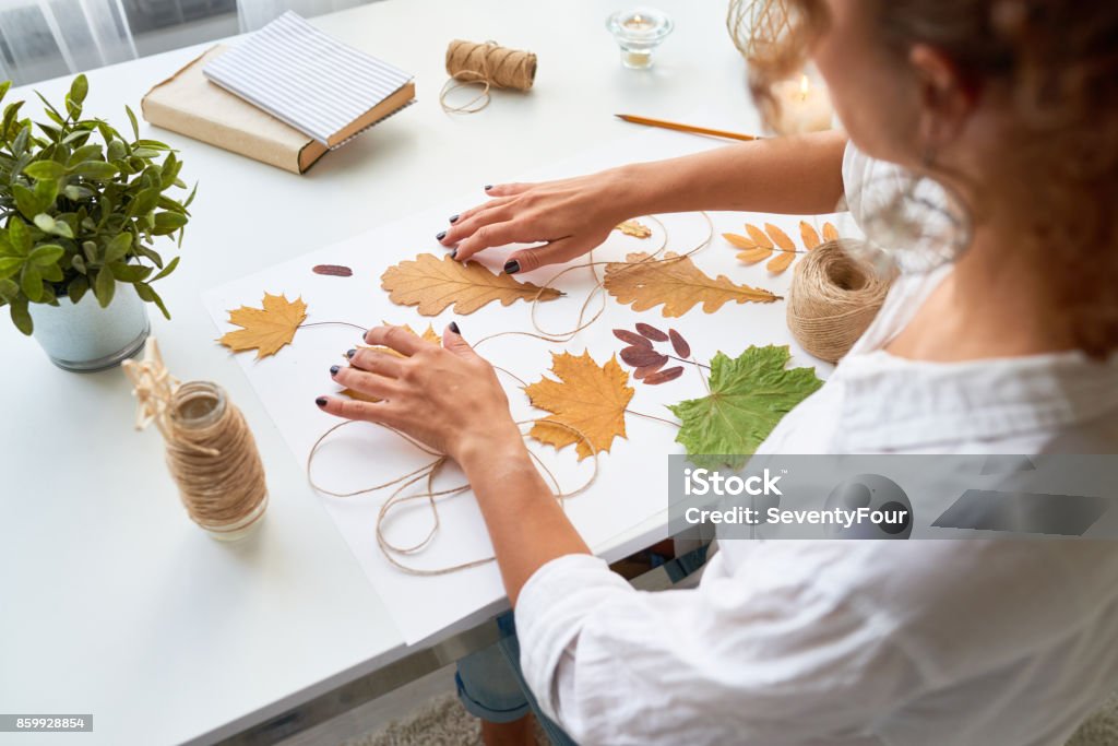 Handmade Autumn Crafts High angle portrait of young woman making handmade autumn decoration using yellow eaves Autumn Stock Photo