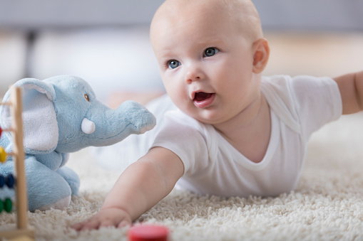 Beautiful baby girl plays with toys at home on the living room floor.