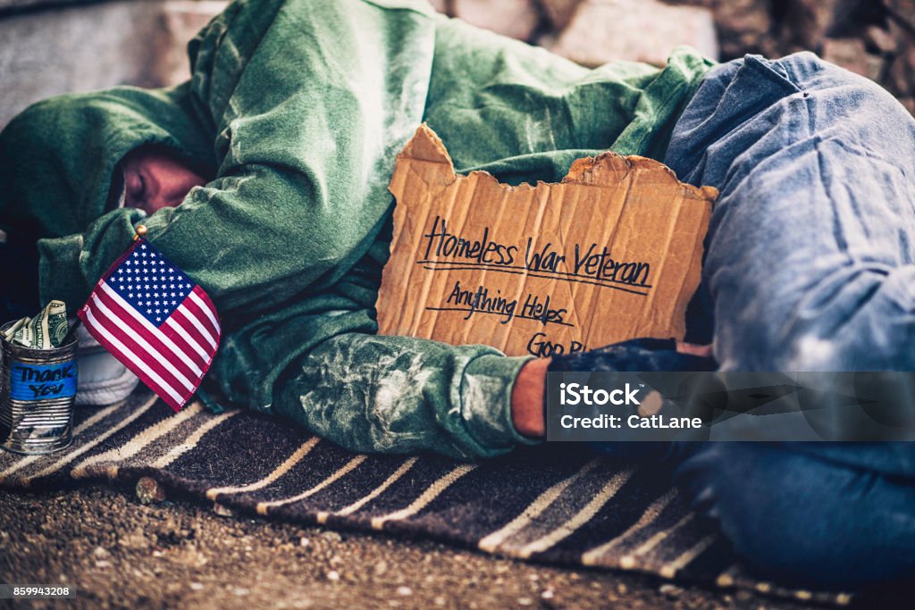 Fighting adversity. Homeless war veteran sleeping with sign and money tin Homelessness Stock Photo