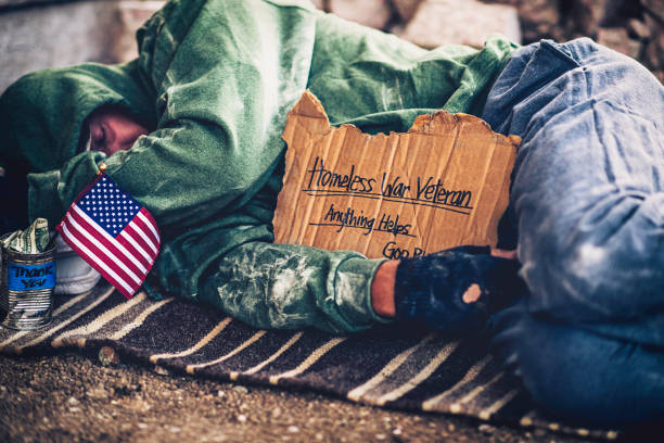 Fighting adversity. Homeless war veteran sleeping with sign and money tin Fighting adversity. Homeless war veteran sleeping with sign and money tin homelessness stock pictures, royalty-free photos & images