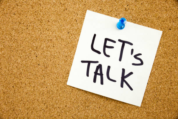 A yellow sticky note writing, caption, inscription Phrase LET'S TALK in black ext on a sticky note pinned to a cork notice board