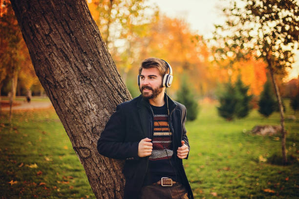 istock Hipster with headphones leaning on the tree in park 859956172