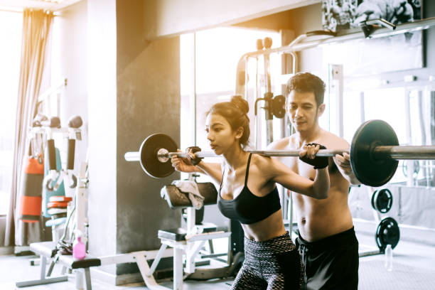 istock Personal trainer helping women and handle heavy barbells two hand top a shoulder. 859967994