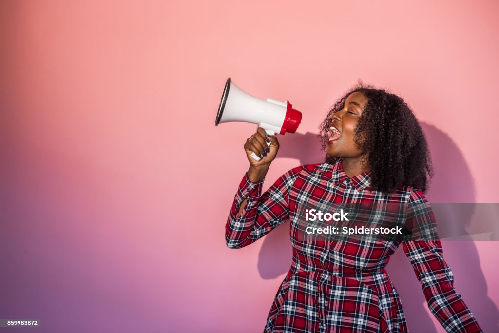 Monochrome -  Black Woman on Pink Background Yells into Megaphone Young black woman standing in front of pink background turns head to side yelling into a megaphone. Megaphone Stock Photo
