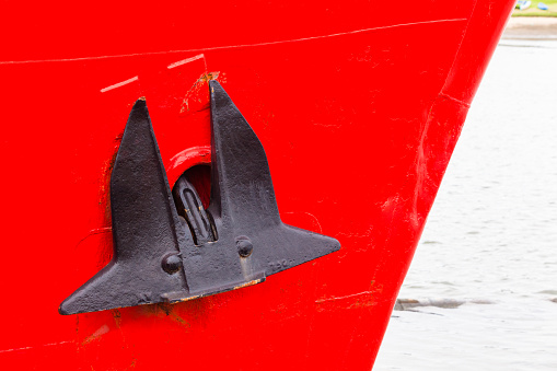 Ship boat bow with anchor black with red paint hull closeup in hatbor port.