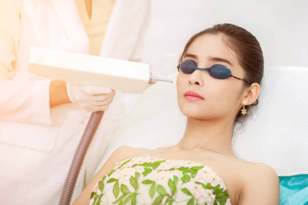 Face Care. Facial Laser Hair Removal. Beautician Giving Laser Epilation Treatment To Young Woman's Face At Beauty Clinic. Body Care. Hairless Smooth And Soft Skin. Asian girl. Health And Beauty Concept. stock photo