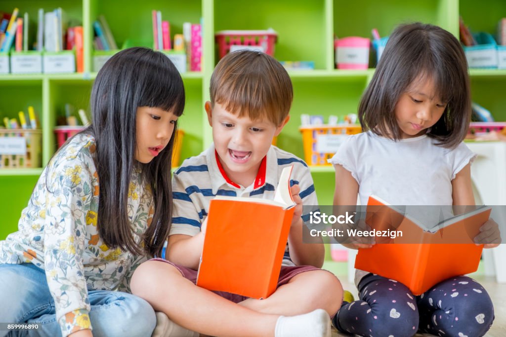 Children sitting on floor and reading tale book  in preschool library,Kindergarten school education concept. Children sitting on floor and reading tale book  in preschool library,Kindergarten school education concept Reading Stock Photo