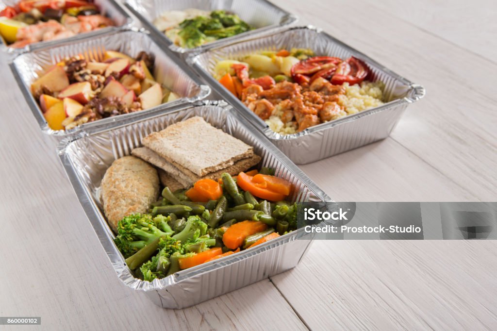 Healthy food take away in foil boxes on wood background Healthy food background. Take away of natural organic meals in foil boxes. Fitness nutrition. Restaurant dishes delivery Delivering Stock Photo