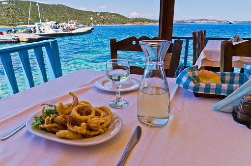 Fried squid and white wine in a shade of a typical greek taverna in a harbour at Amoulani island, Greece