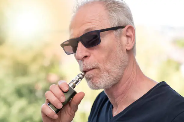 Portrait of mature man smoking an electronic cigarette, light effect