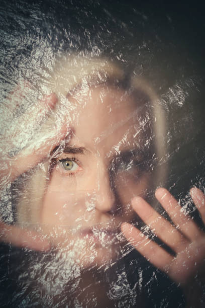 donna che guarda spaventata attraverso il buco in una tenda di plastica trasparente - ghost women caucasian transparent foto e immagini stock