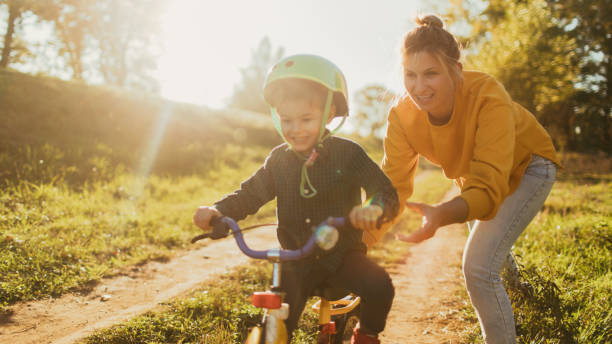 Learning to ride a bicycle Photo of a young boy who is learning to ride a bicycle with a little help from his mother; wide photo dimensions cycling photos stock pictures, royalty-free photos & images