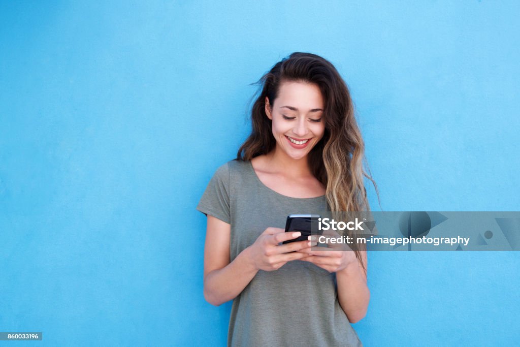 joven sonriente con teléfono móvil contra fondo azul - Foto de stock de Teléfono móvil libre de derechos