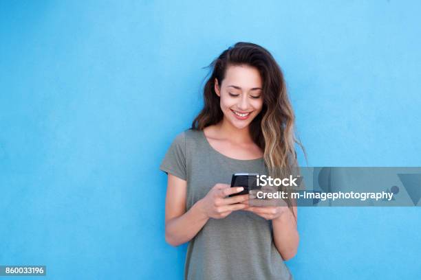 Young Smiling Woman Using Mobile Phone Against Blue Background Stock Photo - Download Image Now