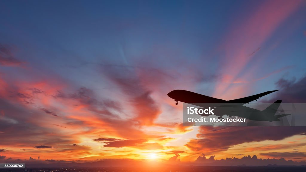 A silhueta de um avião de passageiros voando no pôr do sol. - Foto de stock de Avião royalty-free
