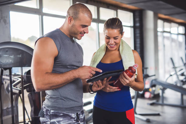istock Young woman discussing workout progress with fitness instructor 860035974