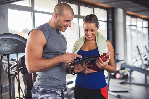Young sporty woman is discussing workout plan, progress and statistics with her fitness instructor using digital tablet.
